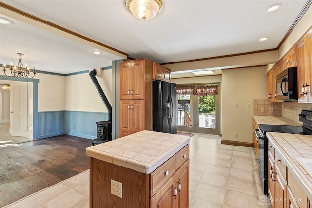 kitchen featuring light wood-type flooring, a kitchen island, black appliances, a wood stove, and tile counters