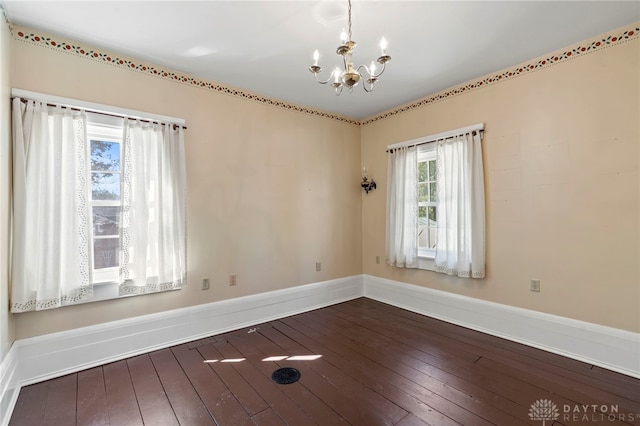 spare room featuring dark wood-type flooring and an inviting chandelier