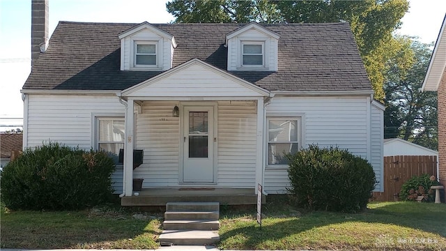 cape cod home with fence, a front yard, and roof with shingles