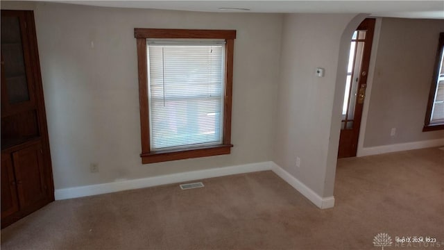 spare room featuring baseboards, visible vents, arched walkways, and light carpet