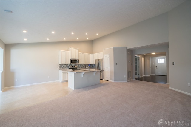 kitchen featuring appliances with stainless steel finishes, backsplash, a kitchen island with sink, white cabinets, and a breakfast bar area