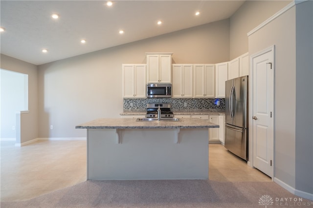 kitchen with decorative backsplash, a kitchen breakfast bar, stainless steel appliances, a kitchen island with sink, and white cabinetry