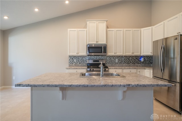 kitchen with lofted ceiling, a kitchen island with sink, white cabinets, a kitchen breakfast bar, and stainless steel appliances