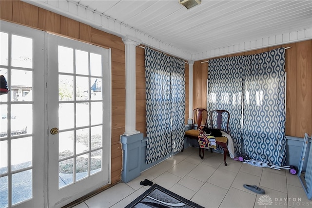 doorway with a wealth of natural light, wood walls, light tile patterned floors, and ornate columns