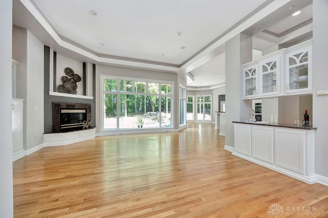 unfurnished living room with light wood-type flooring, a raised ceiling, a premium fireplace, and ornamental molding