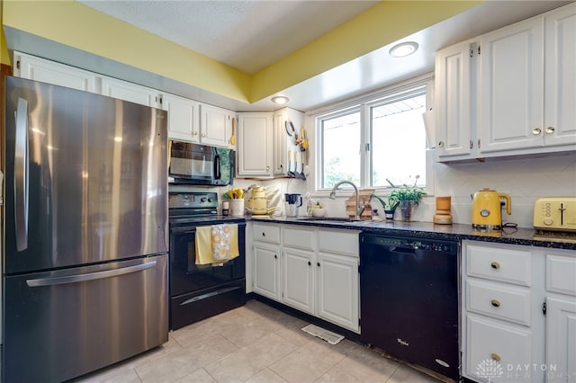 kitchen featuring dark stone counters, sink, black appliances, light tile patterned floors, and white cabinets