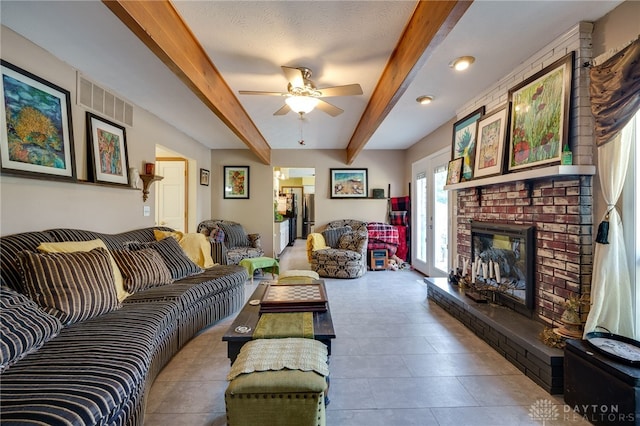 living room with beam ceiling, ceiling fan, a textured ceiling, and a brick fireplace