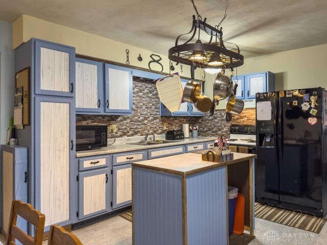 kitchen with hanging light fixtures, tasteful backsplash, a kitchen island, black appliances, and an inviting chandelier