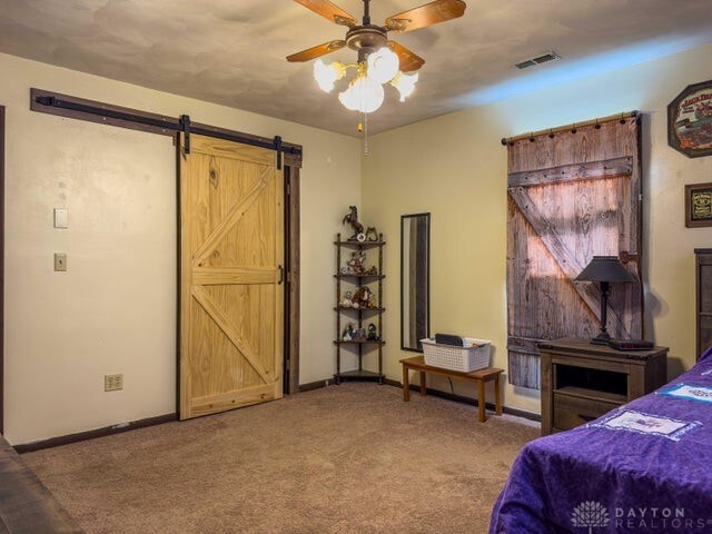 carpeted bedroom with ceiling fan and a barn door