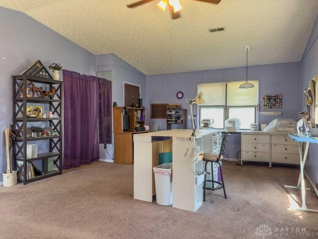 kitchen featuring pendant lighting, vaulted ceiling, light colored carpet, a kitchen breakfast bar, and ceiling fan