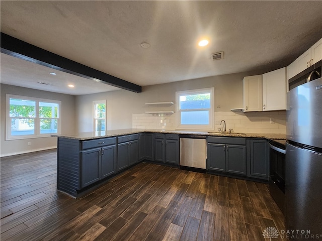 kitchen featuring kitchen peninsula, appliances with stainless steel finishes, dark wood-type flooring, beam ceiling, and white cabinets