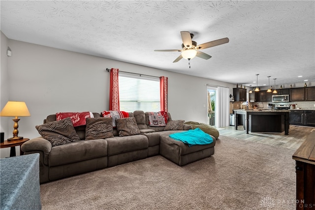 living room with light hardwood / wood-style floors, ceiling fan, and a textured ceiling