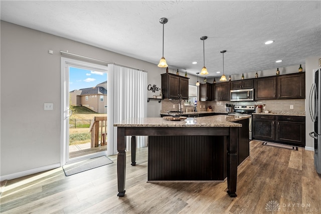 kitchen with light stone counters, hardwood / wood-style flooring, stainless steel appliances, and hanging light fixtures