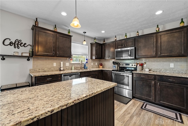 kitchen with appliances with stainless steel finishes, dark brown cabinetry, light hardwood / wood-style floors, and pendant lighting