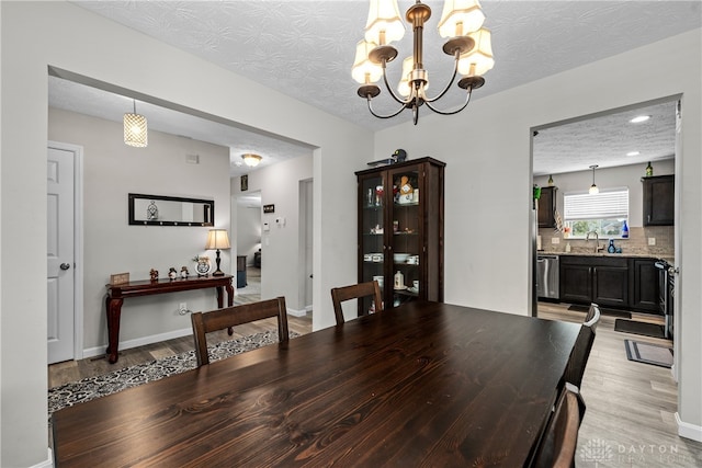 dining room featuring light wood-type flooring, a chandelier, a textured ceiling, and sink