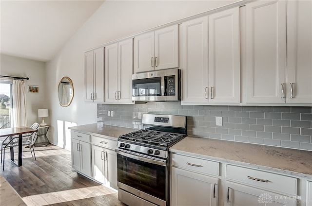 kitchen with light hardwood / wood-style flooring, backsplash, white cabinetry, appliances with stainless steel finishes, and vaulted ceiling