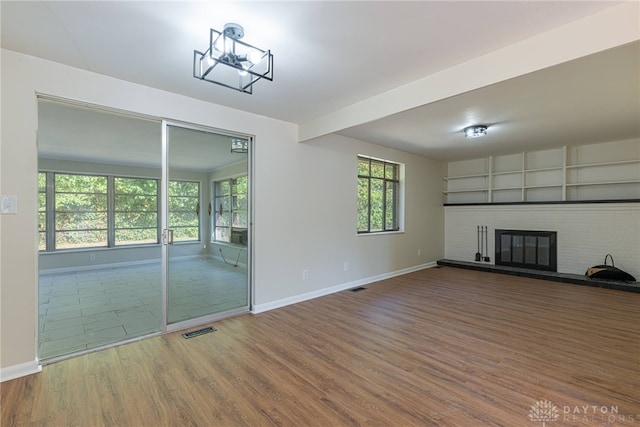 unfurnished living room featuring a brick fireplace, hardwood / wood-style floors, and an inviting chandelier