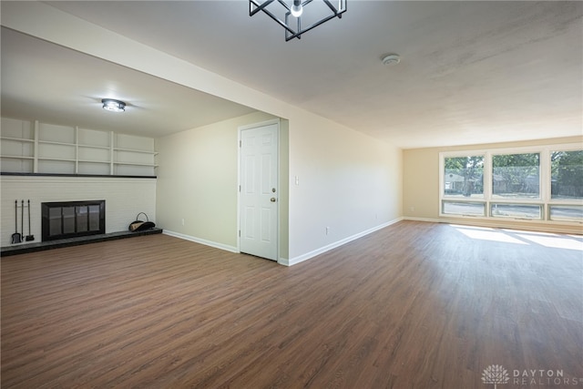 unfurnished living room featuring built in features, a brick fireplace, and dark hardwood / wood-style flooring