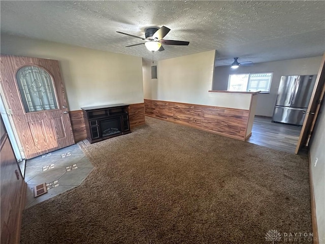 unfurnished living room featuring dark colored carpet, ceiling fan, a textured ceiling, and wood walls