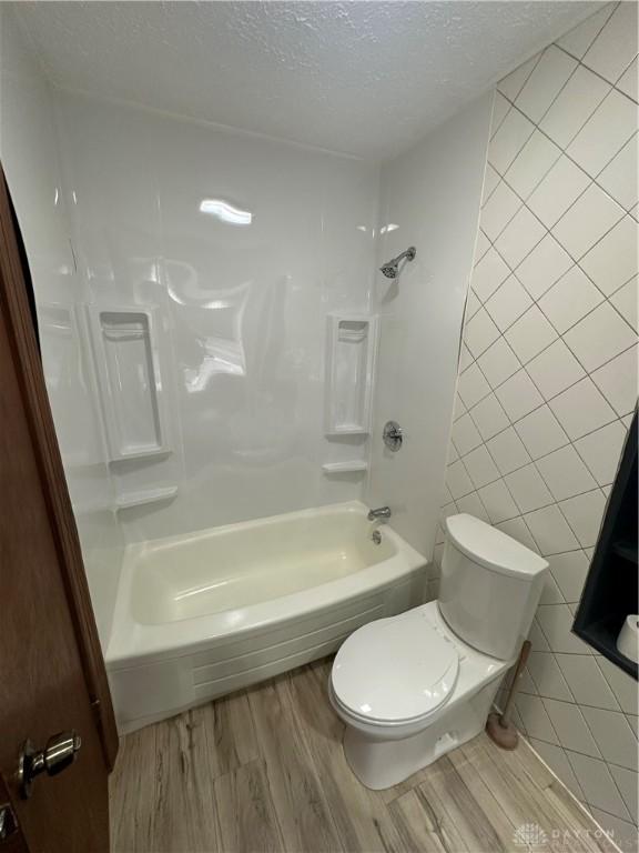 bathroom with toilet, tile walls, shower / bathing tub combination, a textured ceiling, and hardwood / wood-style floors