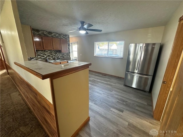 kitchen with tile countertops, stainless steel refrigerator, kitchen peninsula, light hardwood / wood-style floors, and decorative backsplash