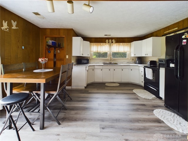 kitchen with wood walls, black appliances, sink, white cabinetry, and light hardwood / wood-style floors