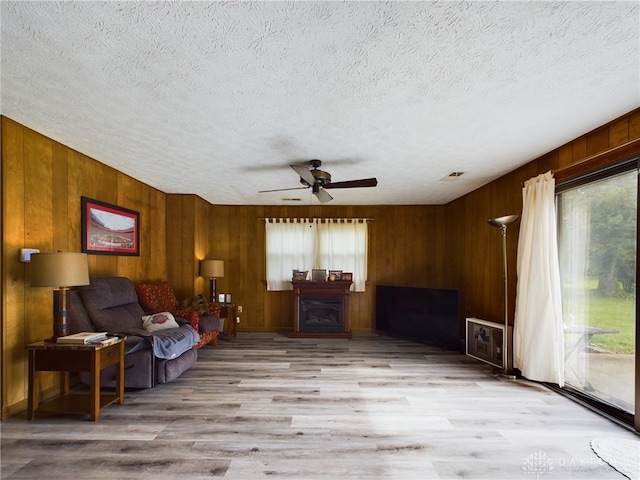 sitting room featuring wood walls, a textured ceiling, light wood-type flooring, and ceiling fan