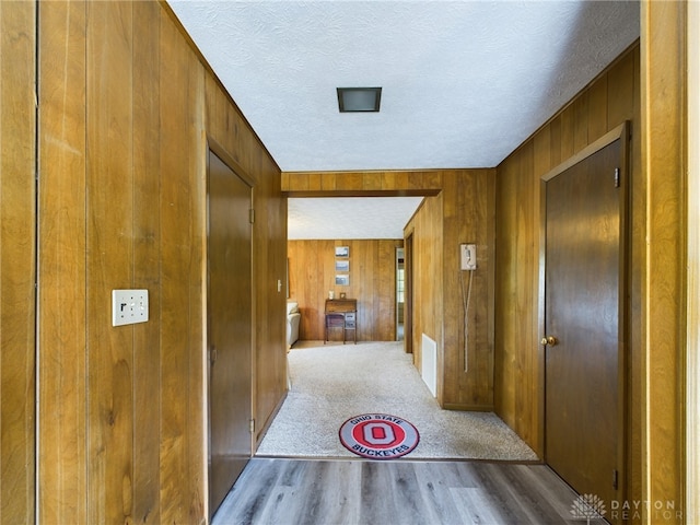 hallway featuring wooden walls, light hardwood / wood-style flooring, and a textured ceiling