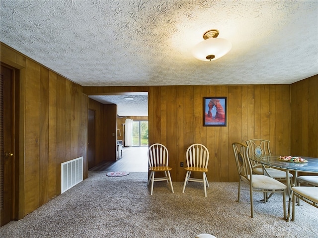 carpeted dining room featuring wood walls and a textured ceiling