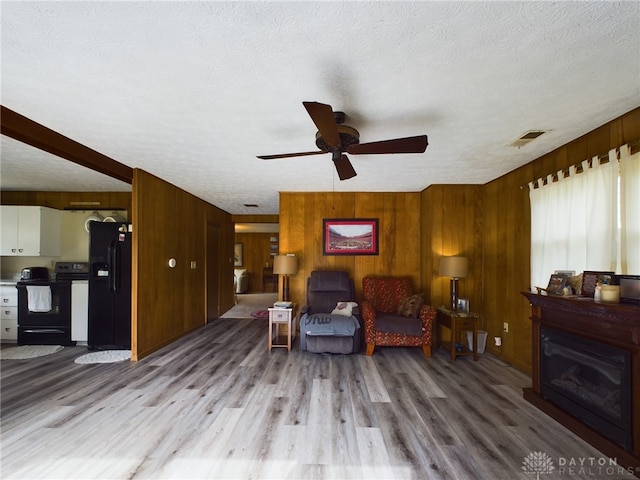 living room with a textured ceiling, ceiling fan, wood-type flooring, and wooden walls