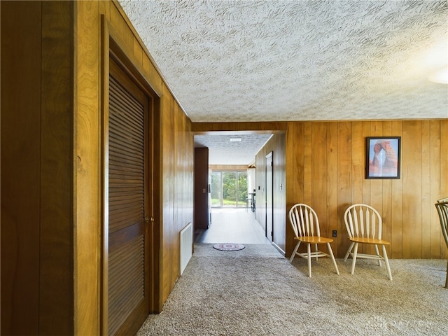 corridor featuring carpet, a textured ceiling, and wooden walls