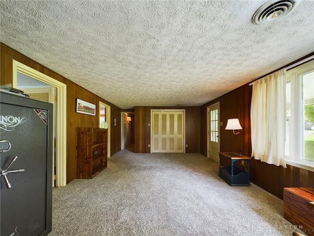 unfurnished living room with a textured ceiling, carpet floors, and wood walls