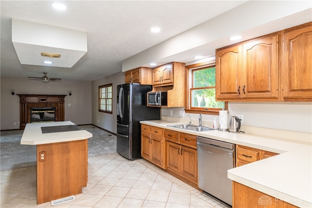 kitchen with a brick fireplace, stainless steel appliances, ceiling fan, sink, and light colored carpet