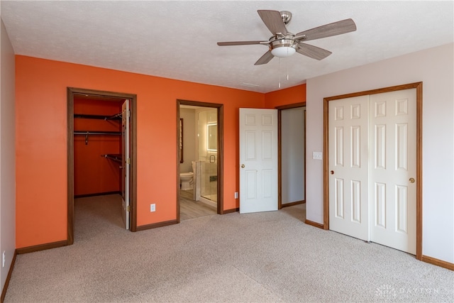 unfurnished bedroom with connected bathroom, a textured ceiling, ceiling fan, a walk in closet, and light carpet