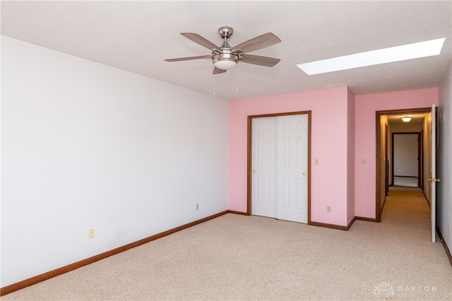 unfurnished bedroom with light carpet, ceiling fan, a skylight, and a closet