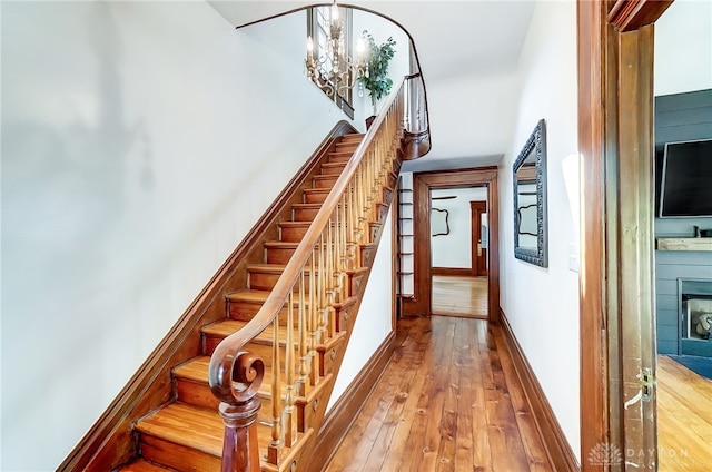 staircase featuring wood-type flooring, a tiled fireplace, and a chandelier