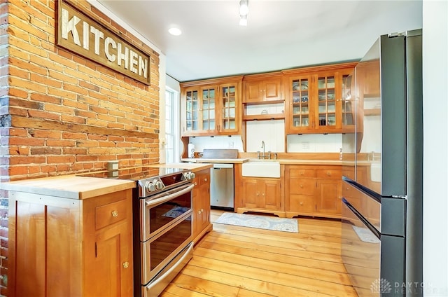 kitchen featuring butcher block countertops, sink, light hardwood / wood-style flooring, stainless steel appliances, and brick wall