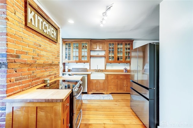 kitchen with light hardwood / wood-style floors, wood counters, sink, stainless steel appliances, and brick wall