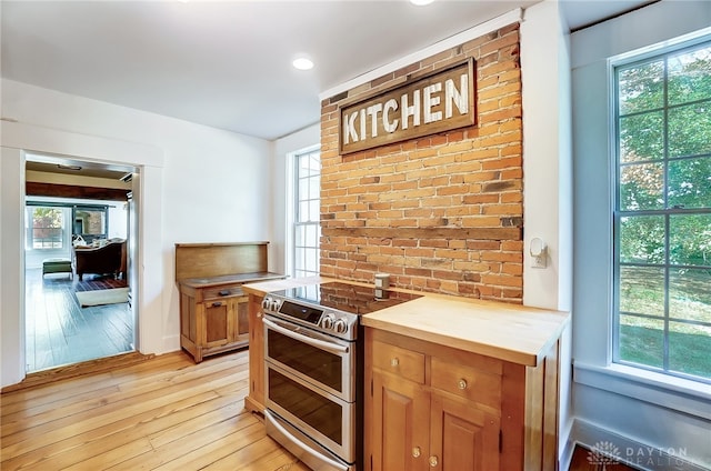 kitchen with brick wall, stainless steel range with electric stovetop, light wood-type flooring, and butcher block countertops