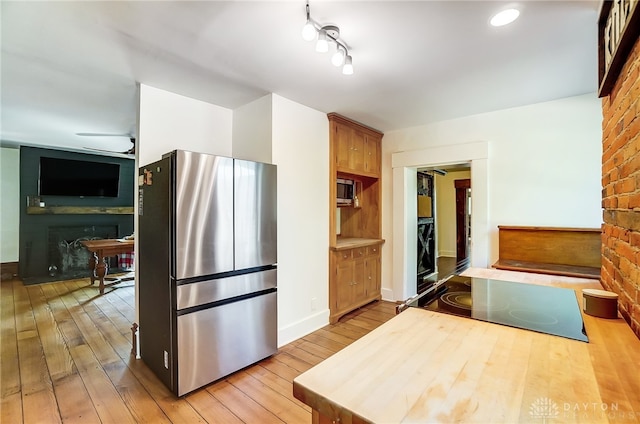 kitchen featuring light wood-type flooring, a fireplace, stainless steel appliances, and brick wall