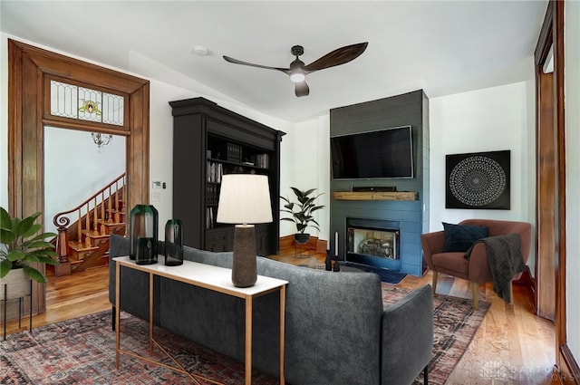 living room featuring wood-type flooring, a large fireplace, and ceiling fan