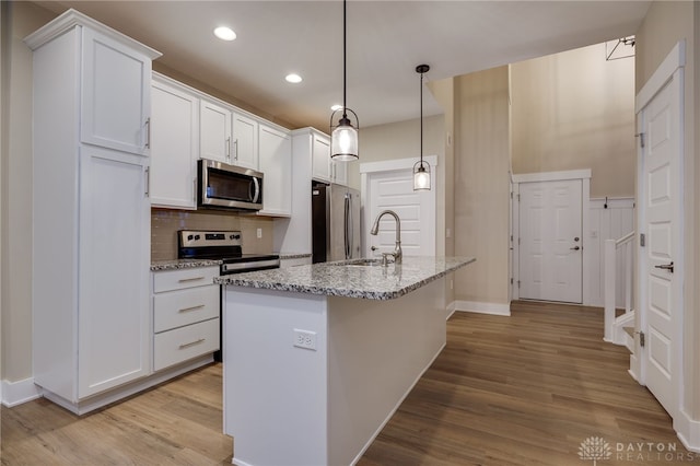 kitchen featuring white cabinets, stainless steel appliances, decorative light fixtures, and light hardwood / wood-style floors