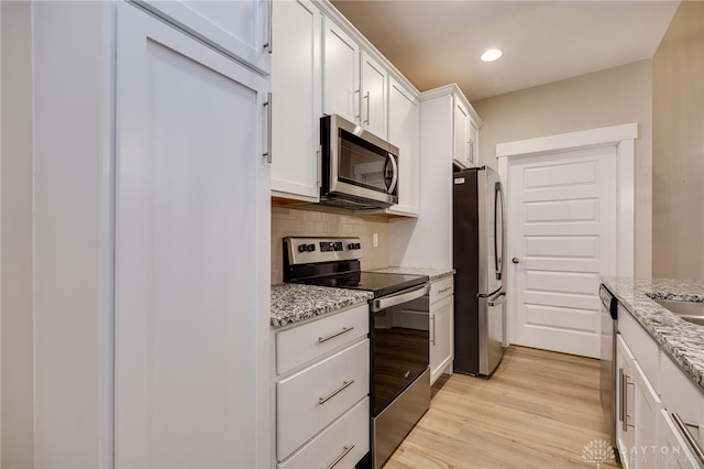 kitchen featuring white cabinets, light wood-type flooring, tasteful backsplash, light stone counters, and stainless steel appliances