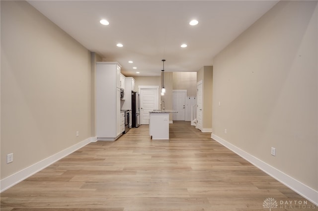 kitchen featuring stainless steel fridge, a center island with sink, hanging light fixtures, and light hardwood / wood-style floors