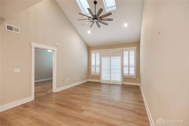 spare room with a skylight, ceiling fan, high vaulted ceiling, and light wood-type flooring