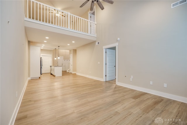 unfurnished living room featuring ceiling fan, light hardwood / wood-style flooring, a towering ceiling, and sink