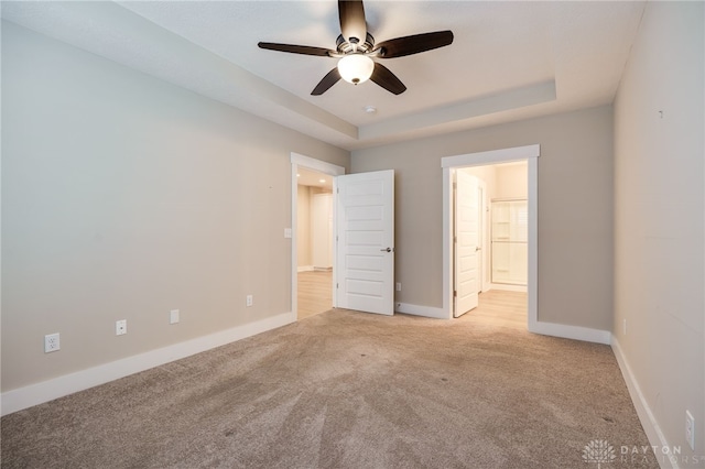 unfurnished bedroom featuring light colored carpet, ceiling fan, and a tray ceiling