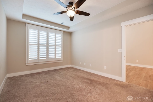 empty room with light carpet, a raised ceiling, and ceiling fan