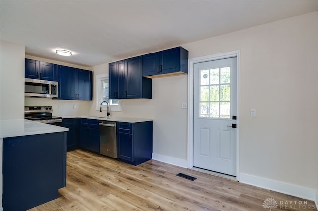 kitchen featuring blue cabinetry, appliances with stainless steel finishes, light hardwood / wood-style flooring, and sink