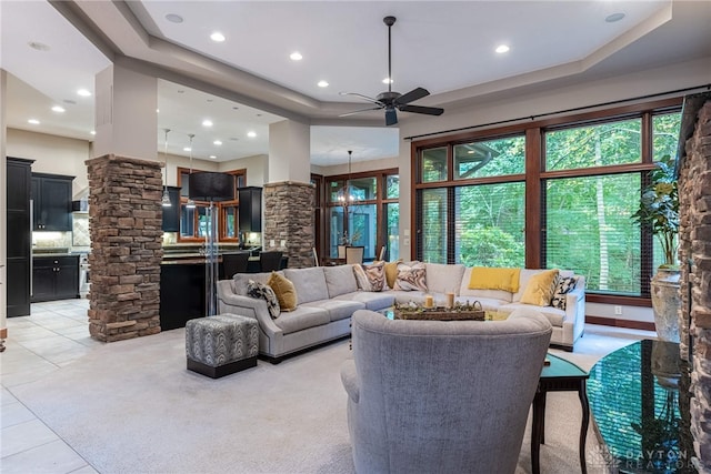 tiled living room featuring ceiling fan with notable chandelier, ornate columns, and a wealth of natural light